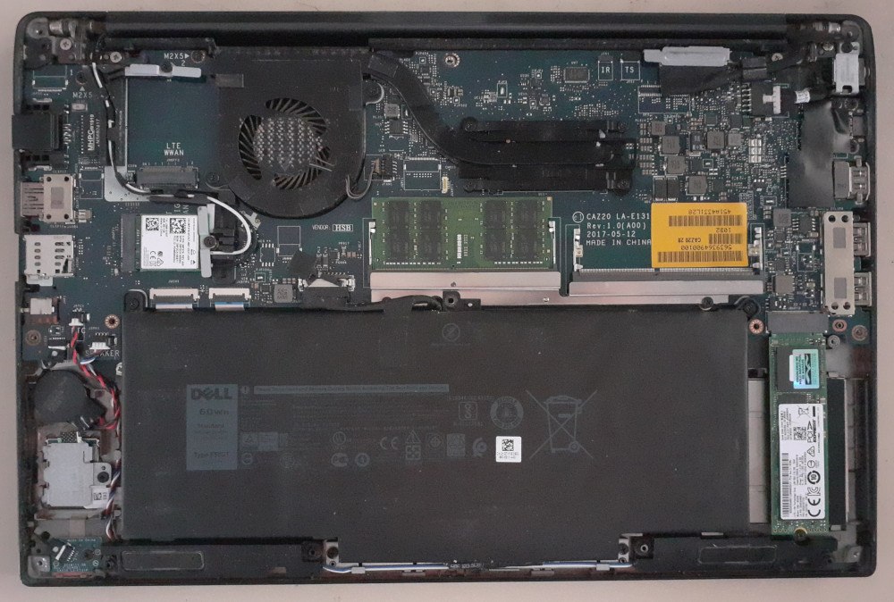 The Dell laptop seen from above, lid closed, with the screen against the desk and the bottom cover removed, exposing the motherboard.